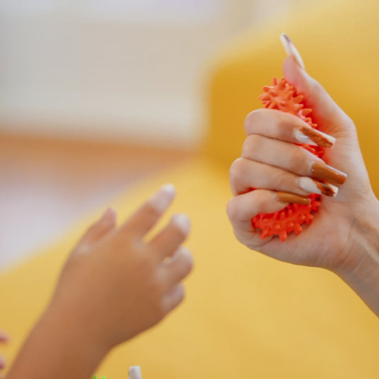 Video showing hedgehog spiky sensory rings in blue, green and orange, and a girl playing with them at a desk